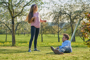 Young couple on a meadow between apple trees in spring laughing happily at each other and having fun