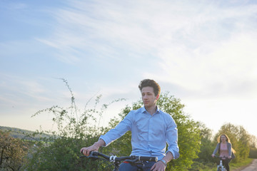 Young couple riding bicycle in greenery, young man in the foreground young woman in the background