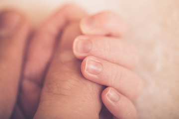 Touch of love. Close-up of baby's hand holding mother's finger. Newborn baby holding mother's hand, image with shallow depth of field.