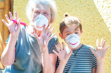 Happy laughing grandmother with grandchild in a respiratory masks plays together near house. Family...