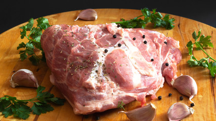 a fresh piece of pork meat placed on a wooden Board and seasoned with pepper, garlic, and parsley