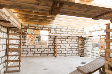 Building site of a house under construction. Unfinished house walls made from white aerated autoclaved concrete blocks. Scaffolding for workers assembled from boards and Euro-pallets.