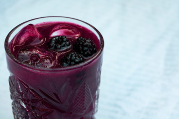 A mouth-watering purple blackberries bramble cocktail on a white, slightly textured background. © Roksana Tomasiak