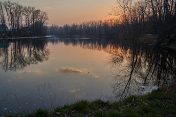    Early spring. Morning dawn over the lake in a misty, thoughtful haze. Beautiful view of the forest covered with fog early in the morning. The sun's rays of light.       