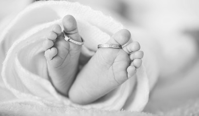 Legs of a newborn baby with mom's wedding ring in a warm white wool rug. Happy Family concept....