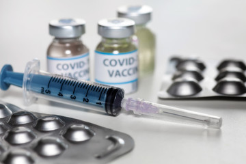 Injection syringe with vaccine bottles and medicine in selective focus for treatment of COVID-19 patients