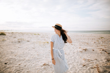 Fototapeta na wymiar Happy young woman in a hat walks on the sea beach