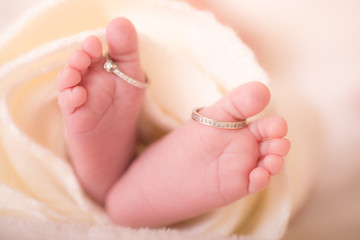 Feet of a newborn and his parents wedding rings. Legs of a newborn baby with mom's wedding ring in a warm white wool rug. Happy Family concept. Beautiful conceptual image of Maternity.