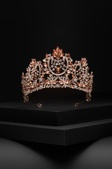 Subject shot of a golden tiara adorned with a lot of peach colour gems and clear sparkling...