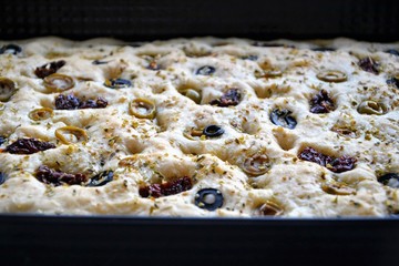 Delicious home made focaccia bread with black olives, green olives, dried tomatoes and herbs. Traditional Italian focaccia - homemade flat bread in the baking tray.