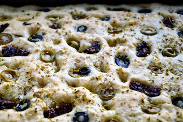 Delicious home made focaccia bread with black olives, green olives, dried tomatoes and herbs. Traditional Italian focaccia - homemade flat bread.Closeup, selective focus