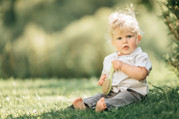 Cute little baby boy sitting on the grass in summer, on a Sunny day. Selective focus, space for text