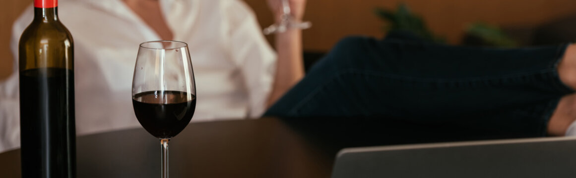 selective focus of glass and bottle of red wine near woman, cropped view, horizontal image