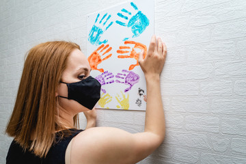 Beautiful girl in black medical mask hangs a canvas picture with her hands on a brick wall background. danger of the virus.