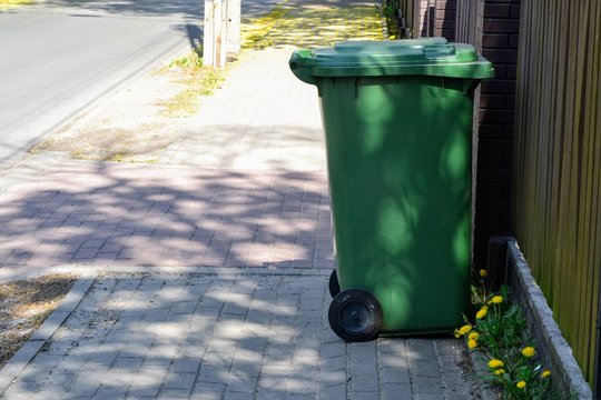 Green plastic garbage can or trash  disposal bin on wheels. Trash bin on the pavement. Space for text. Garbage collection, ecology concept