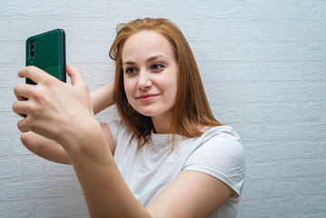 Naklejka premium Beautiful young woman in casual wear is making a selfie using a smart phone and smiling.