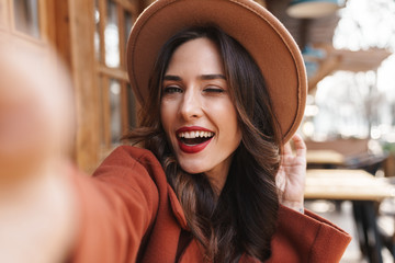 Image of joyful elegant adult woman winking and taking selfie photo