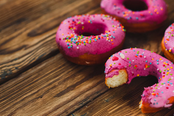 Homemade bitten doughnuts pink with rainbow sprinkles and one white with icing poppy seeds on the right side wooden background. Free copy space. Top view