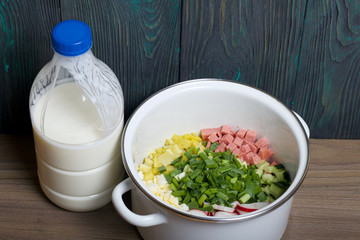 Okroshka with kefir. Russian dish. Sliced vegetables are visible in the pan. Nearby is a bottle of kefir.