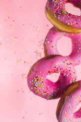 Homemade circle pink donuts with rainbow sprinkles are flying in the air levitate motion on the trendy pink background isolated. Close up top view macro shoot