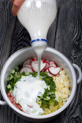 Sliced vegetables in a pan. Kefir is pouring from the bottle. Okroshka with kefir. Russian dish.
