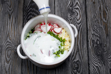 Sliced vegetables in a pan. Kefir is pouring from the bottle. Okroshka with kefir. Russian dish.