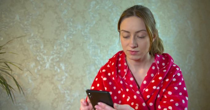 girl in a bathrobe holding a smartphone and taking a home selfie