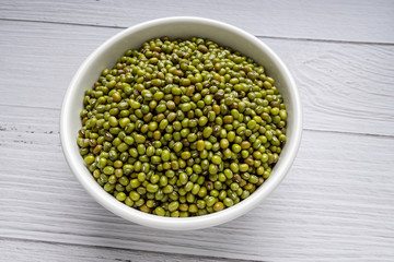 Green mung beans in white bowl on white wood background. top view. vegan food concept
