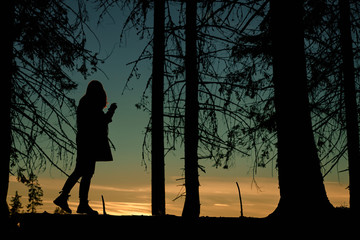 Silhouette of a woman in the forest looking at a sunset/sunrise.