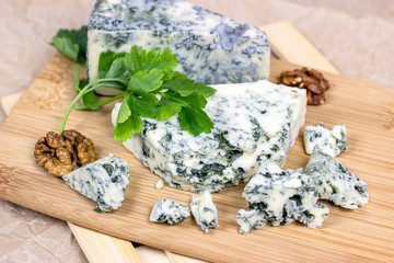 Slices and triangles of Danish Blue (dorblue) cheese with mold on a light wooden board  background.