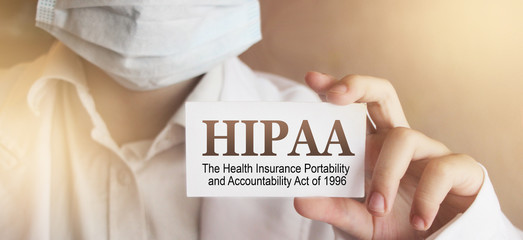 Doctor wearing face mask shows a card with the text HIPPA, The Health Insurance Portability and...