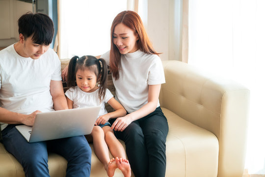 Happy young Asian girl with her lovely parents using laptop computer for education and spent quality time together. Asian family, Social Distancing, homeschooling, work from home or new normal concept