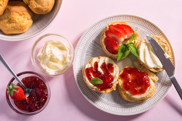 Tasty breakfast of scones with clotted cream and jam on pink background