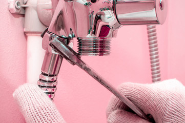 Plumber hands fixing shower mixer on modern water tap. Fun repair, pink walls in the bathroom, selective focus.