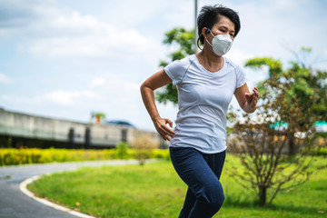 Asian woman wearing face mask while she running in public park after coronavirus outbreak and city lockdown a new normal life. social distancing, new normal, covid-19 or running concepts