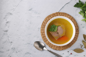 Bouillon from homemade chicken with vegetables, pepper and bay leaf in white bowl on a marble background. Healthy eating concept. View from above