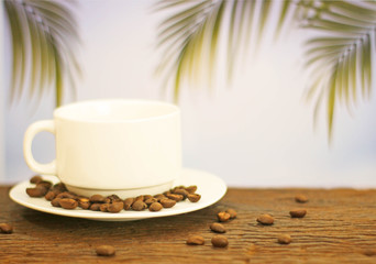 a cup of coffee on wood on blurred palm leaf background