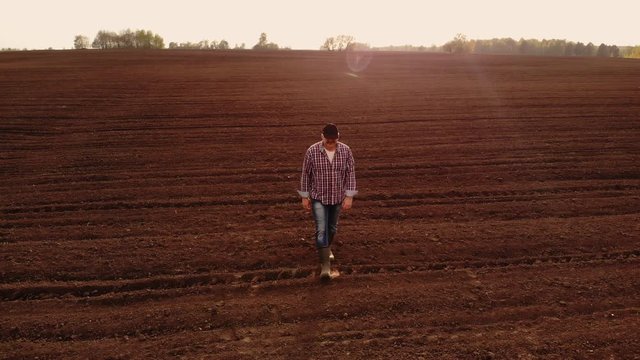 aerial photography the drone follows a farmer walking through a plowed field with land. Fly around and follow farmers top view