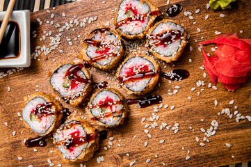 Fried rolls with cucumbers and red caviar.
Wood background. White cup with sauce. Chinese chopsticks