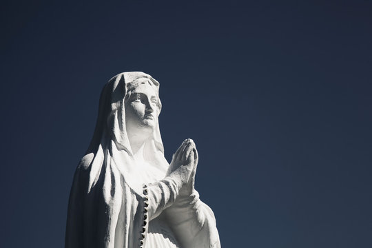 Ancient White Statue Of Virgin Mary Against Blue Sky With Free Copy Space For Text.