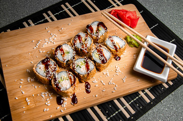 Fried rolls with cucumbers and chicken.
Wood background. White cup with sauce. Chinese chopsticks