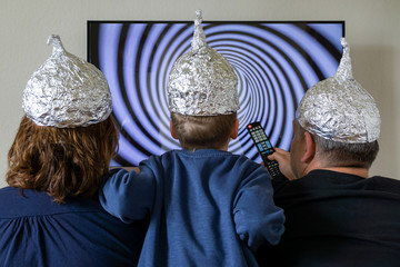 Family looks at the TV and has aluminium hats