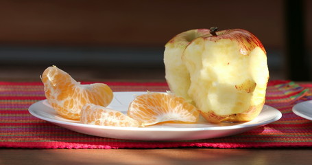 Half eaten apple on plate outside with tangerine fruit