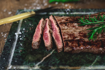Close-up of sliced beefsteak cooked on the grill. Spiced with rosemary and coarse salt. Soapstone surface and a knife. 