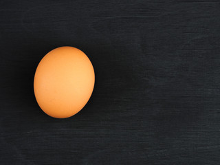 One brown chicken egg on a black wooden background. Healthy eating concept