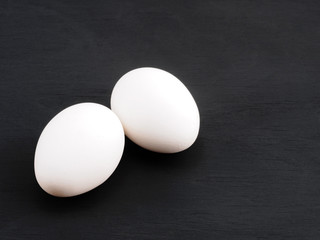 Two white chicken eggs on a black wooden background. Healthy eating concept