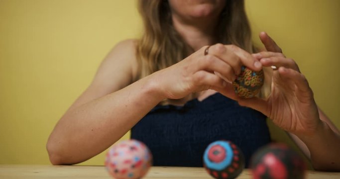 Young woman decorating Easter eggs against a yellow background