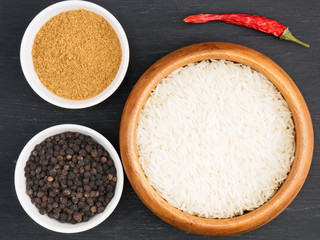 Basmati long, rice, black pepper, masala, hot red chili pepper on black wooden background. Healthy eating and organic food concept