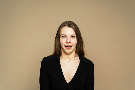 A shoked girl is shruging. A girl is open-eyes on the brown background. A girl with hands in the face