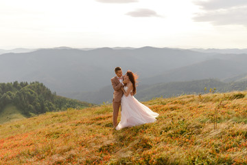 The bride and groom are hugging. Sunset. Wedding photo on a background of autumn mountains. A strong wind inflates hair and dress.